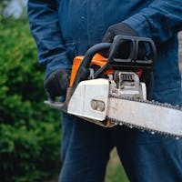 Close-up of a worker holding a chainsaw, ideal for carpentry and outdoor renovations, captured outdoors.